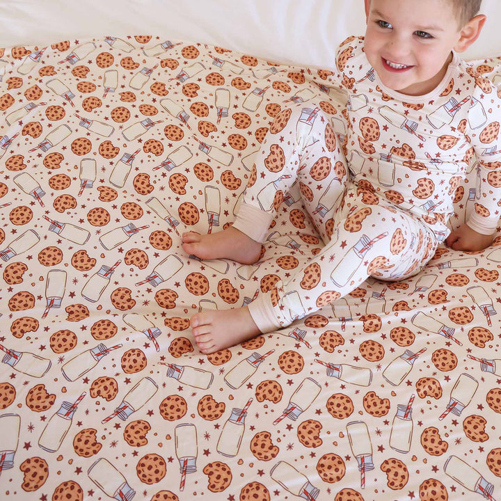 bow wearing milk and cookies two piece pajama set sitting on matching bamboo blanket 