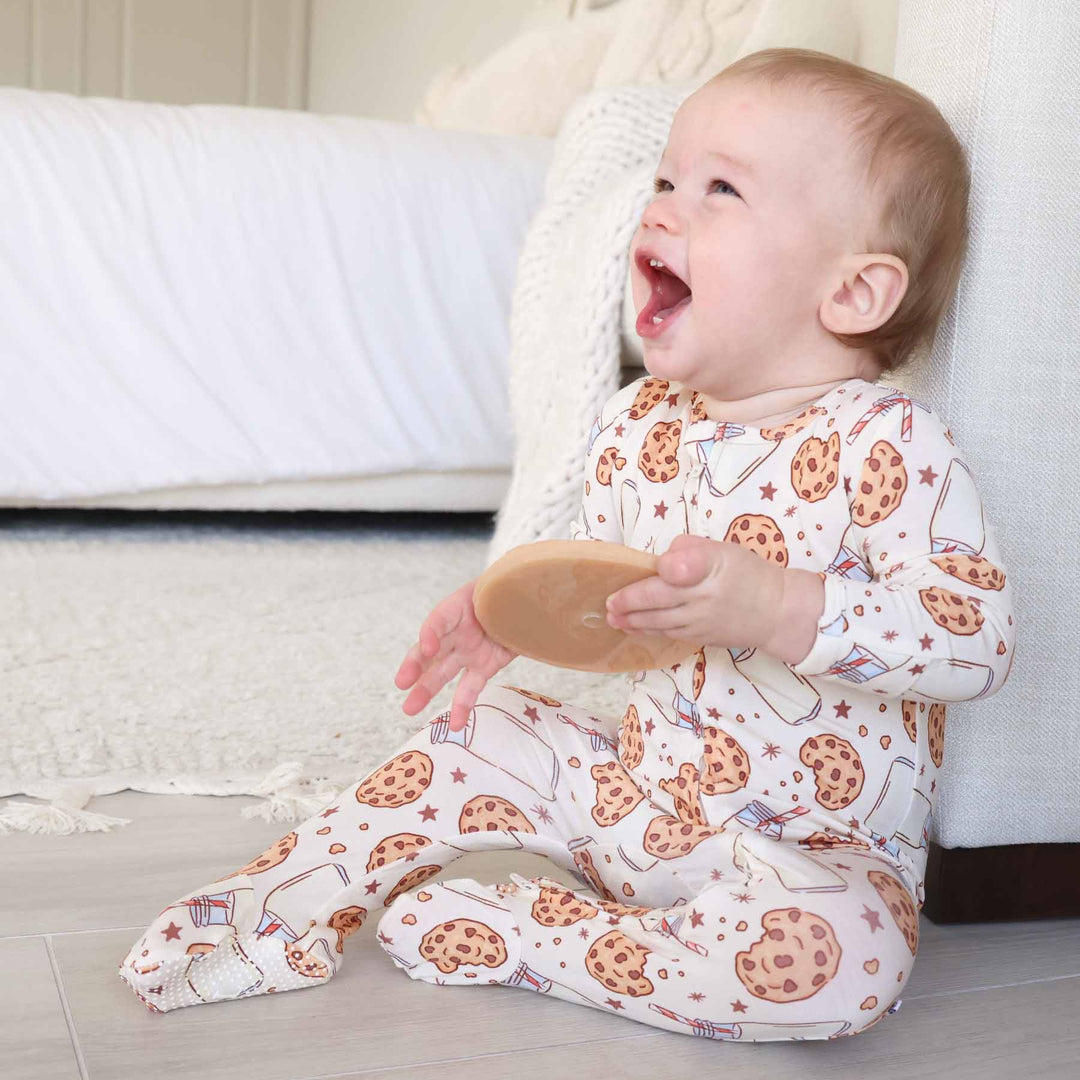 sitting baby wearing a milk and cookie pajama romper holding fake cookie