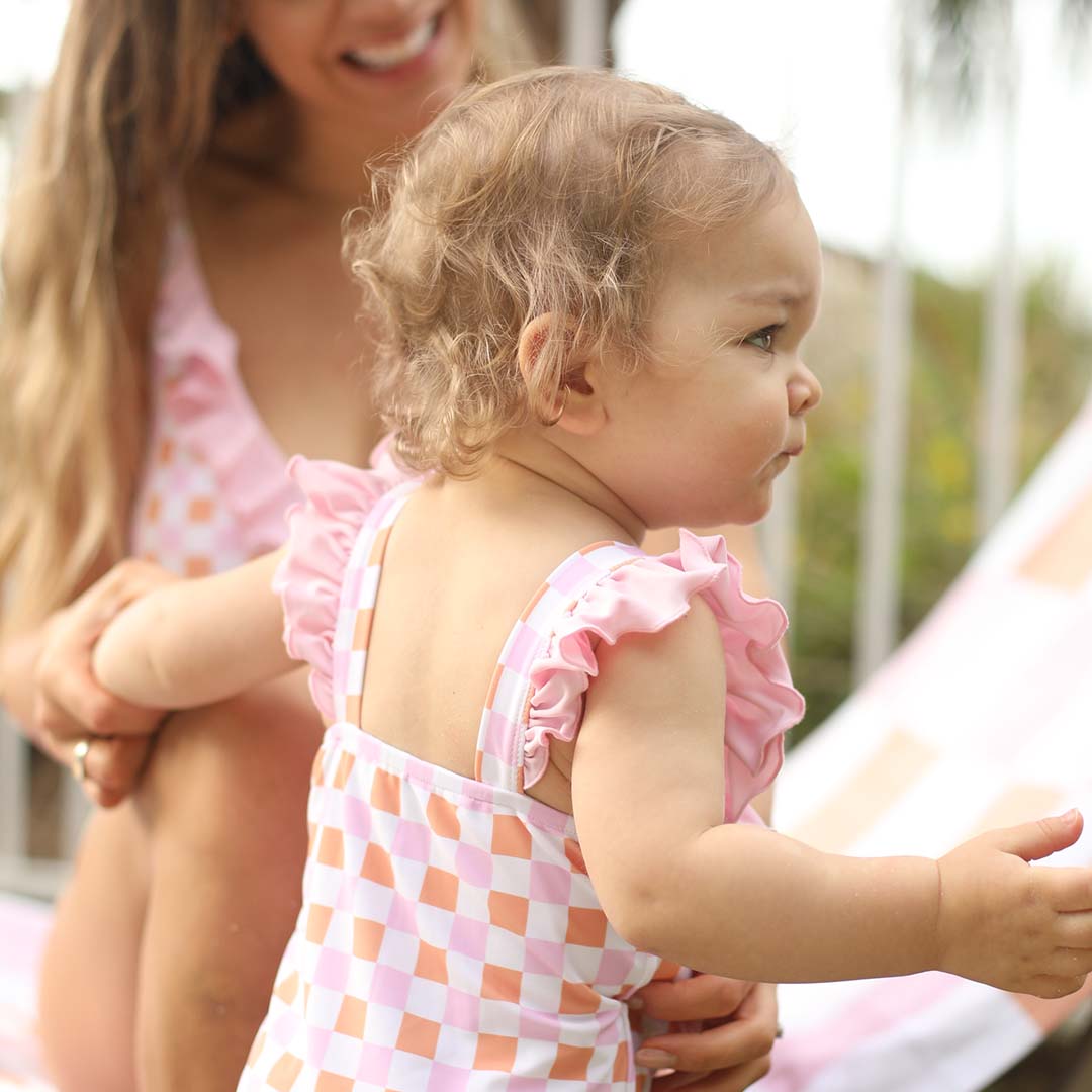 pink ruffled one piece for kids with pink and orange checkered print 