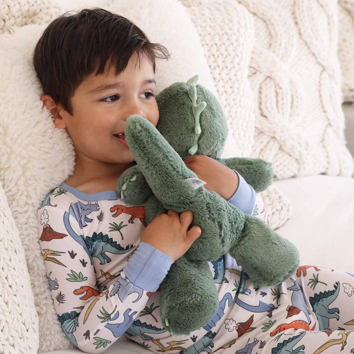 boy in dinosaur pajama set hugging green dinosaur stuffed animal