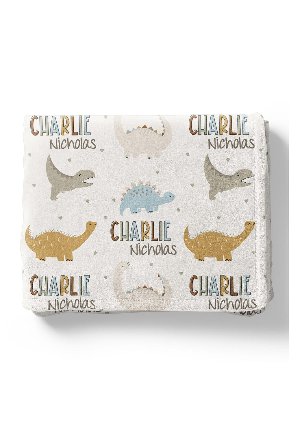 Flat lay of a folded personalized Caden Lane Dino Stomps blanket in cream, showing dinosaur silhouettes, hearts, and custom name print