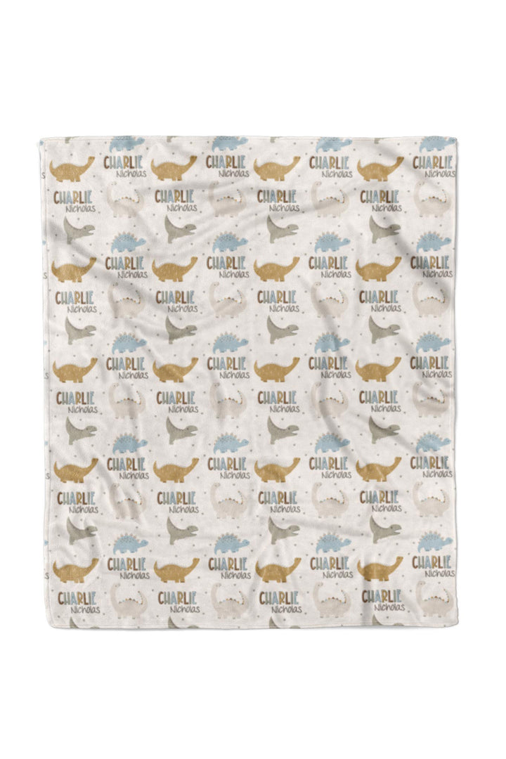 Flat lay of a fully unfolded personalized Caden Lane Dino Stomps blanket in cream, showing the full repeating pattern of dinosaur silhouettes and custom name