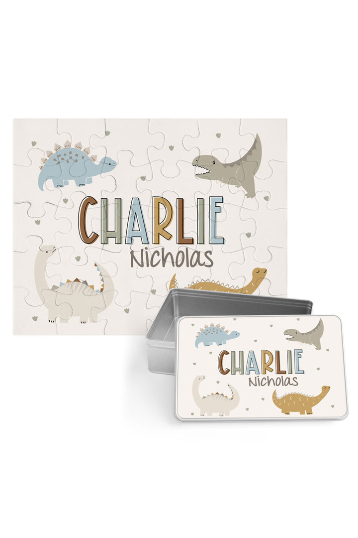 Personalized Caden Lane Dino Stomps jigsaw puzzle in cream, showing dinosaurs and custom name, paired with a matching silver storage tin