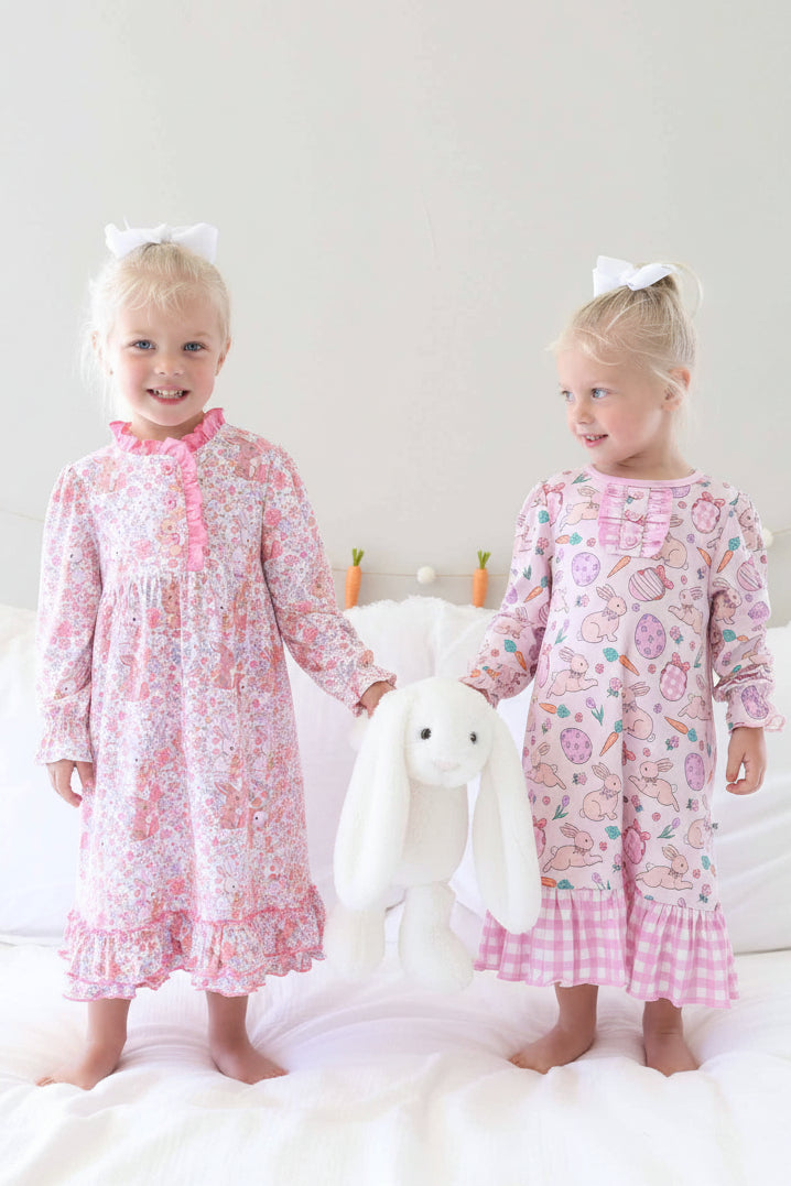 girls standing on bed in long sleeve easter nightgown holding a pink stuffed bunny 