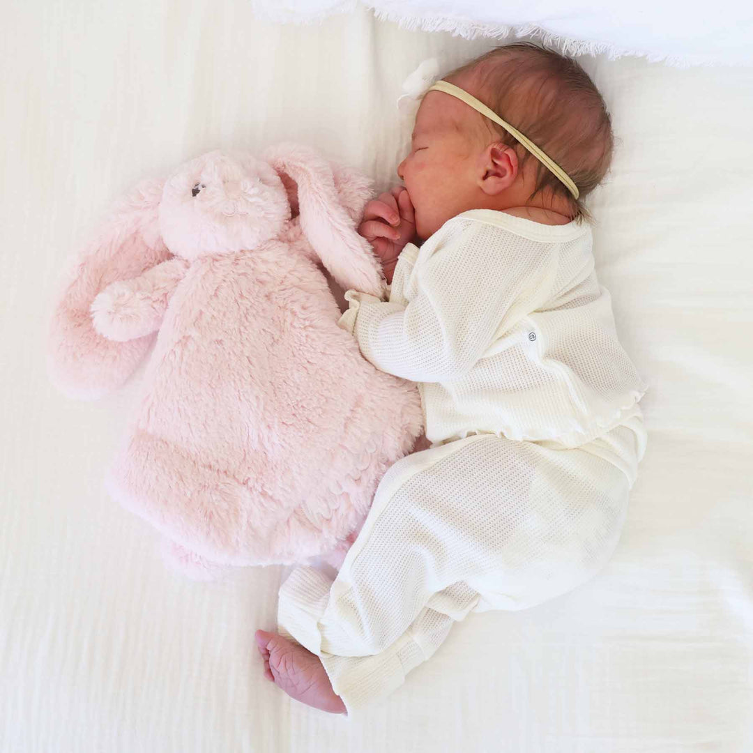 baby laying on side next to a light pink stuffed animal bunny lovey embroidered with name in white thread with script font 