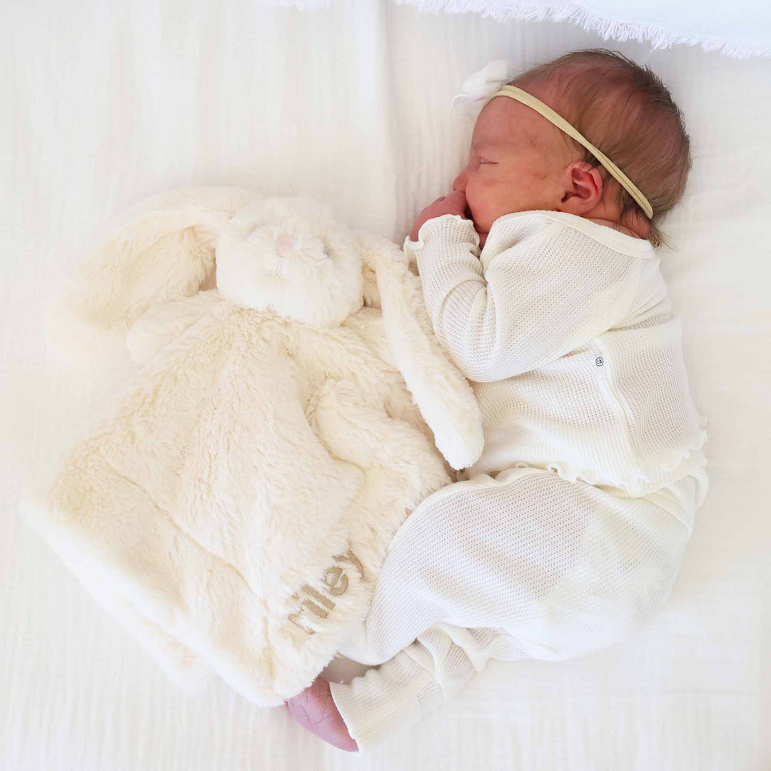 baby laying on side next to a white stuffed bunny lovey embroidered with name 