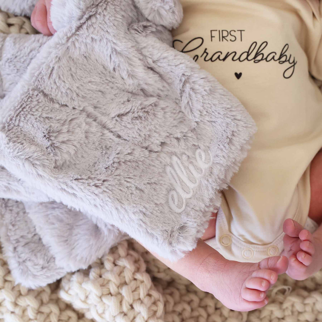 closeup of baby holding a grey elephant plush lovey embroidered with name with white thread in script font 