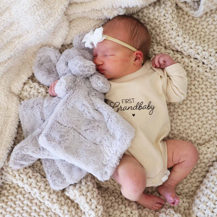 baby laying on blanket holding an elephant plush lovey embroidered with name 