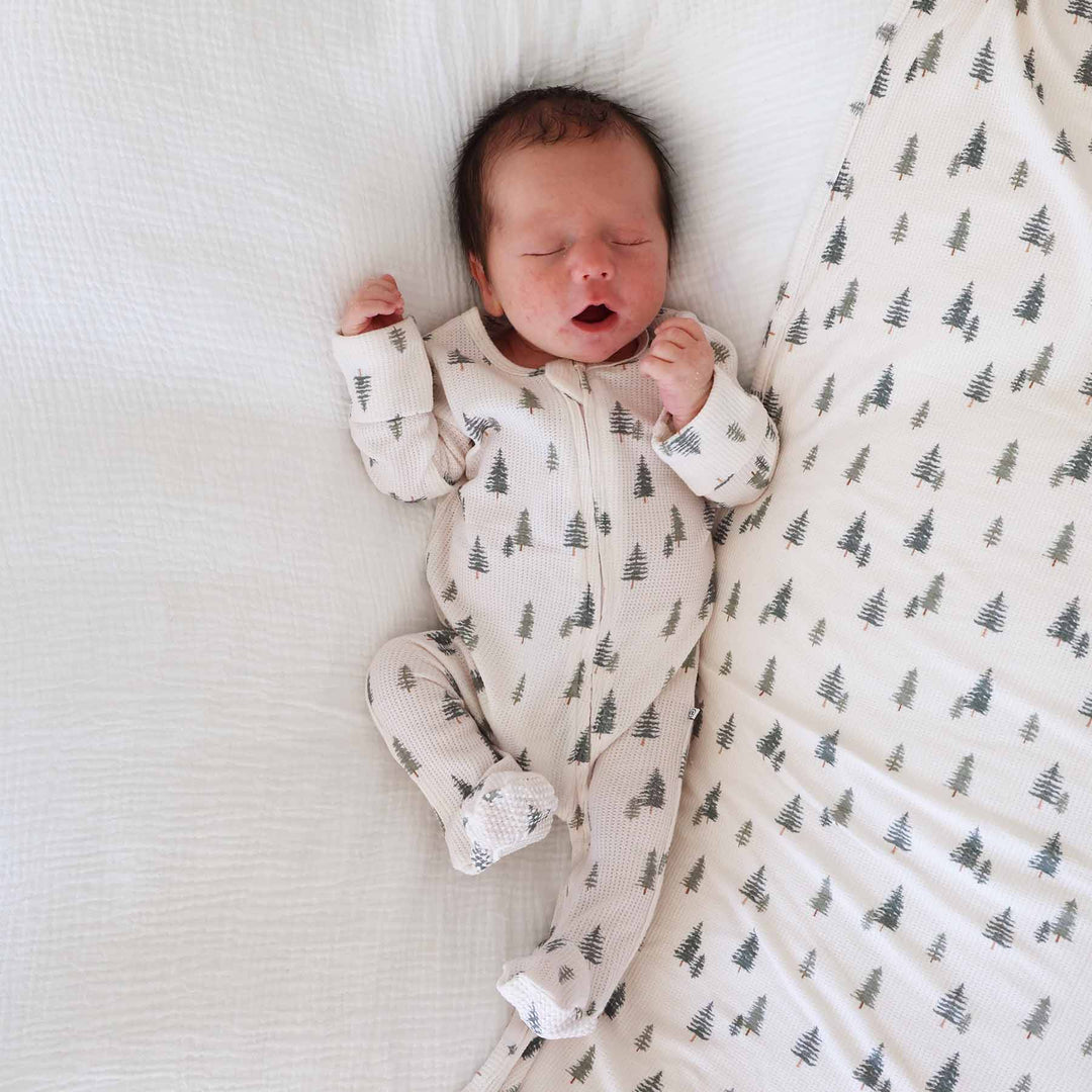 baby laying down wearing pin tree bamboo waffle zipper footie on matching swaddle blanket 