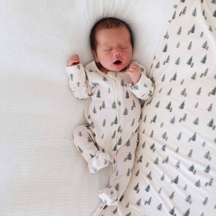 baby laying down wearing pin tree bamboo waffle zipper footie on matching swaddle blanket 