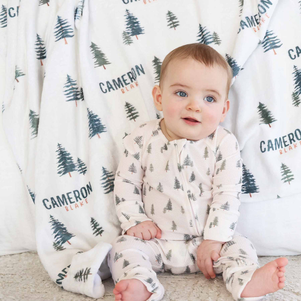 baby wearing evergreen tree bamboo waffle convertible zip romper with matching personalized minky blanket in the background 