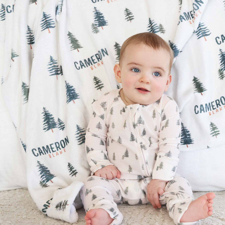 baby wearing evergreen tree bamboo waffle convertible zip romper with matching personalized minky blanket in the background 