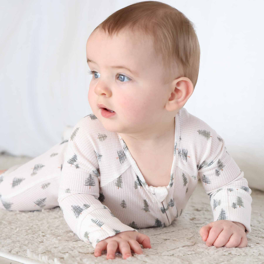 baby laying and wearing the evergreen controvertible zip romper. Green pine trees with white background 
