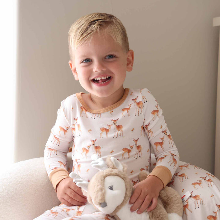 Child dressed in brown and white fawn pajamas cuddling a deer plush toy