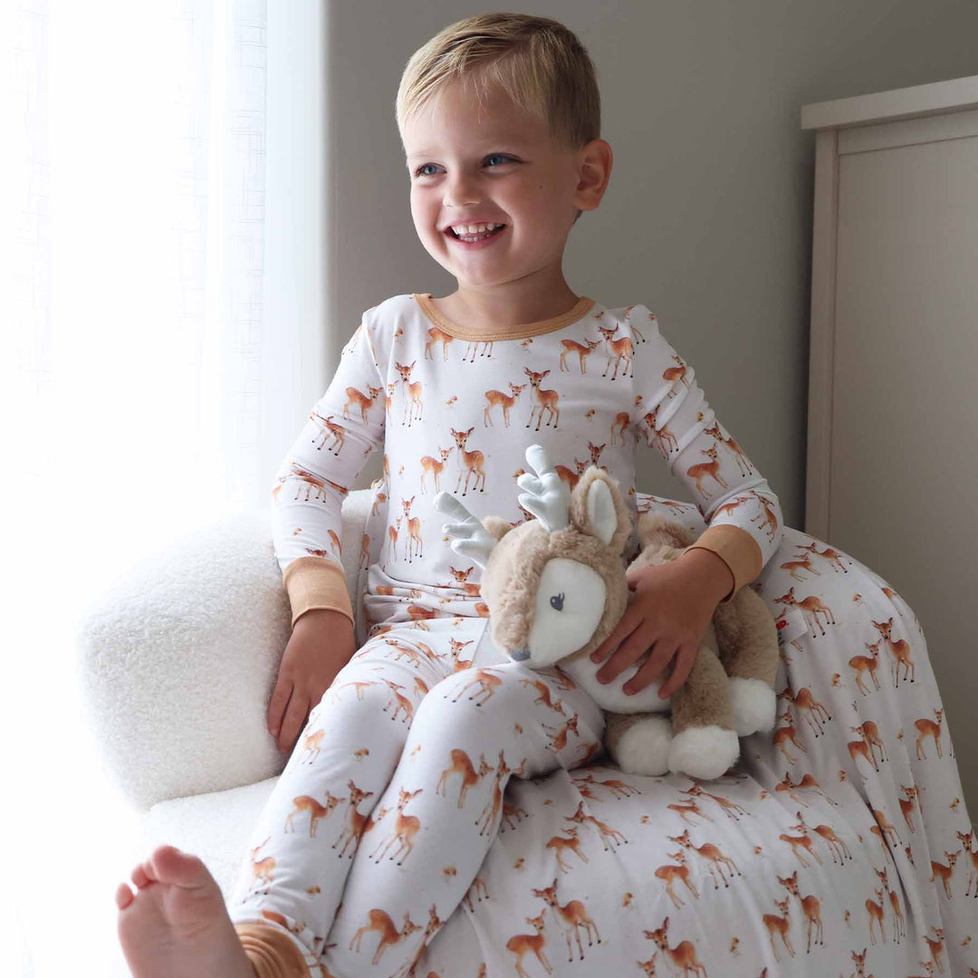 boy wearing a long sleeve fawkn two piece pajama set holding a deer stuffed animal 