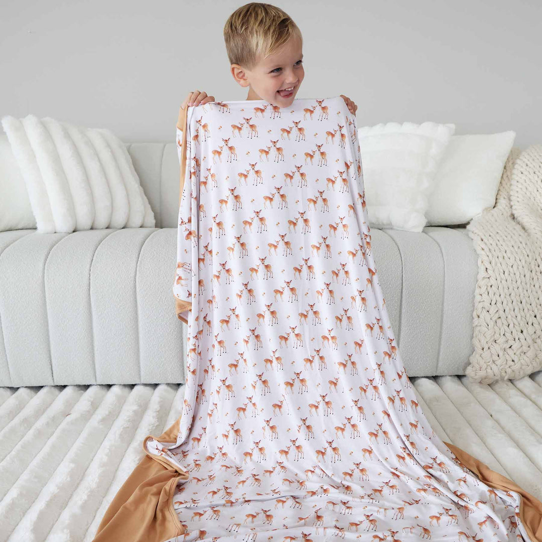 boy holding up a white bamboo blanket with rust colored fawn 