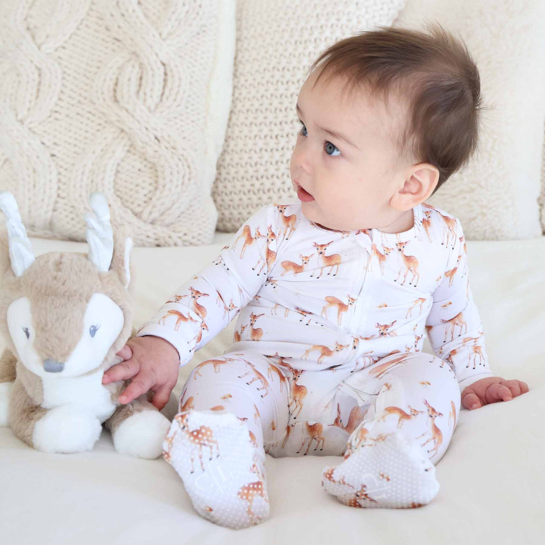 baby sitting on bed in deer zipper footie pajama with deer stuffed animal