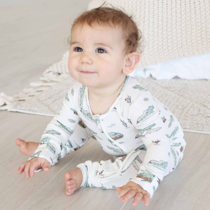 baby boy sitting on floor wearing a tan convertible zip romper pajama with alligators floating on logs and lily pads