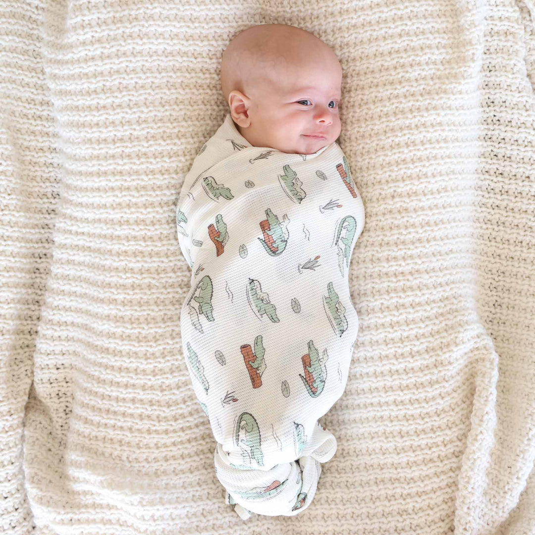 tan swaddle blanket with alligators floating on logs with lily pads and cattails made of bamboo waffle fabric 