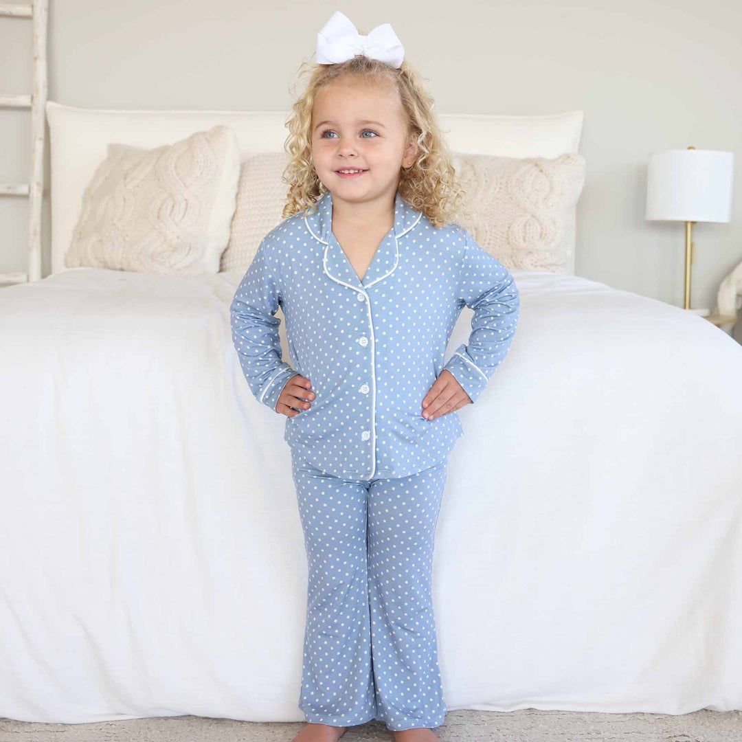little girl standing with hands on hips wearing a two piece lounge set that is blue with white polka dots with flare pants and a collar 