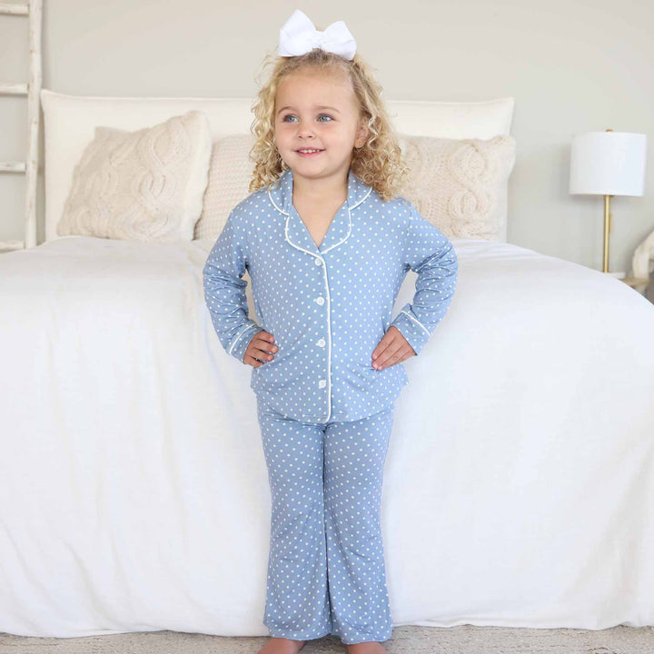 little girl standing with hands on hips wearing a two piece lounge set that is blue with white polka dots with flare pants and a collar 