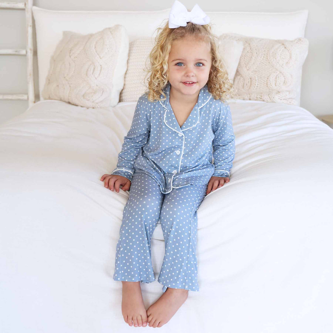 girl sitting on bed wearing a long sleeve collared button up blue lounge set with flare pants that is blue with white polka dots 