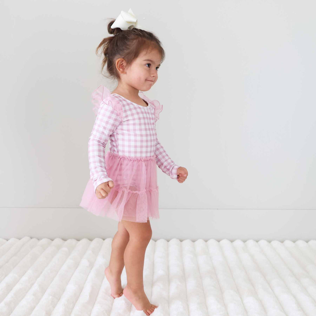 toddler girl standing on toes wearing a long sleeve pink and white gingham leotard 