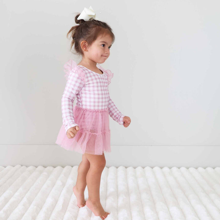 toddler girl standing on toes wearing a long sleeve pink and white gingham leotard 