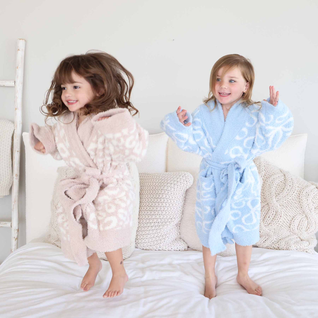 two grils jumping on a bed in a neutral leopard and blue bow robes