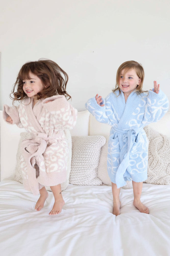two grils jumping on a bed in a neutral leopard and blue bow robes