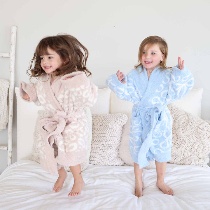 two grils jumping on a bed in a neutral leopard and blue bow robes