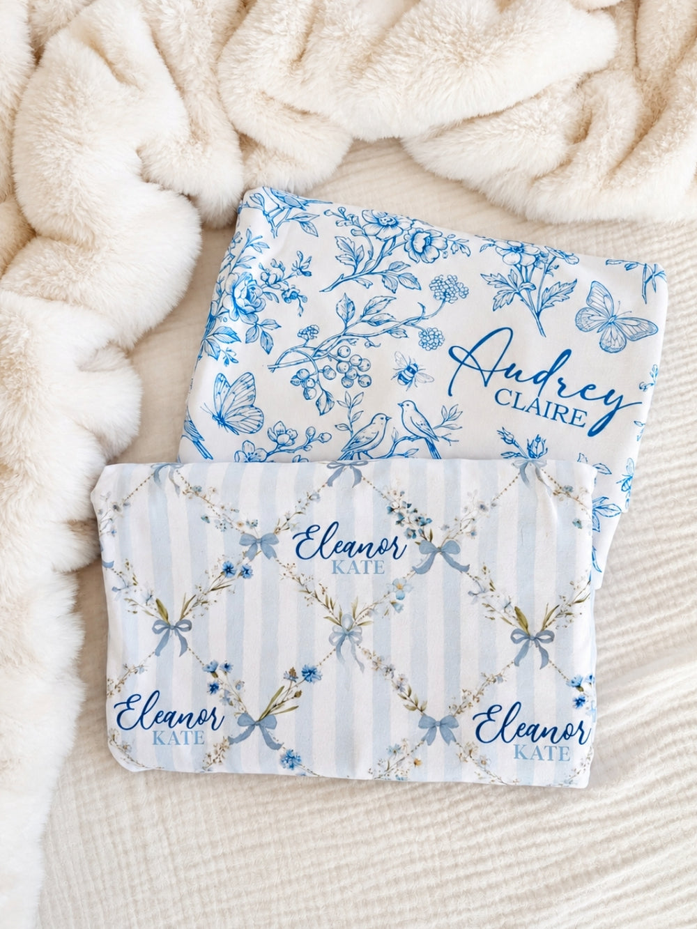 Flat lay of a Caden Lane light blue knit swaddle in a Garden Trellis print featuring stripes and blue bows, reading "Eleanor Kate," paired with a blue toile swaddle.