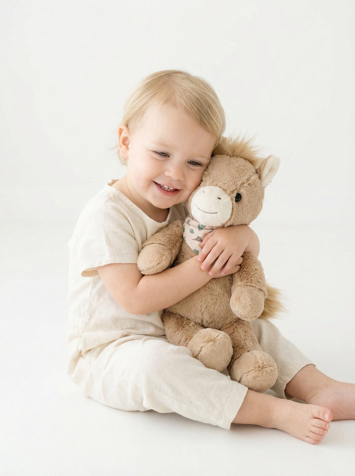 boy in pony club pajamas cuddling peanut pony plush on bed