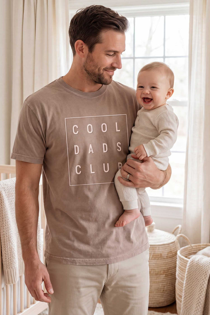 dad holding baby wearing the cool dads club graphic tee