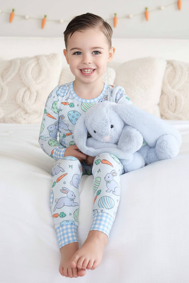 boy wearing long sleeve and pant blue hoppy spring easter two piece pajama set for boys holding a blue stuffed bunny 