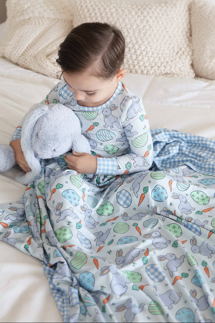 boy wearing a pastel blue two piece pajama set for kids with a matching double sided bamboo blanket with gingham backing 