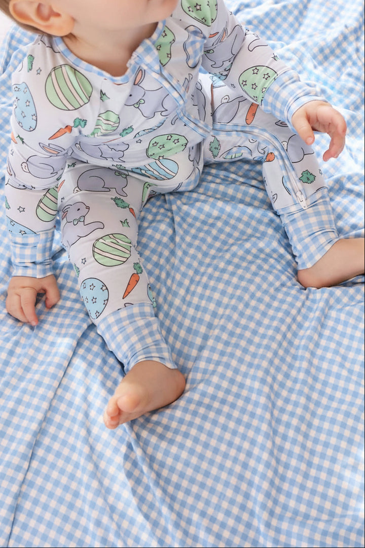 baby boy sitting on a blue and white gingham double sided bamboo blanket wearing a blue easter egg, bunny and carrot convertible zip romper 