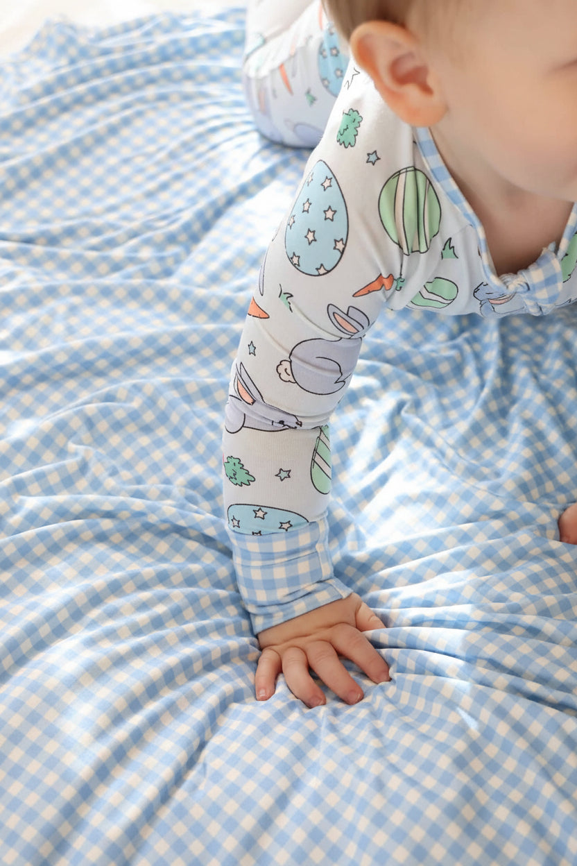 baby boy wearing a blue easter egg, bunny and carrot convertible zip romper pajama with blue and white gingham accents crawling on a blue and white gingham bamboo blanket 