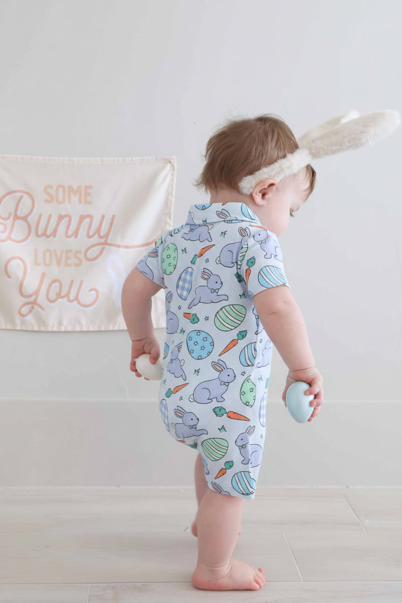 boy wearing the blue hoppy spring short sleeve collared romper with bunny ears holding easter eggs