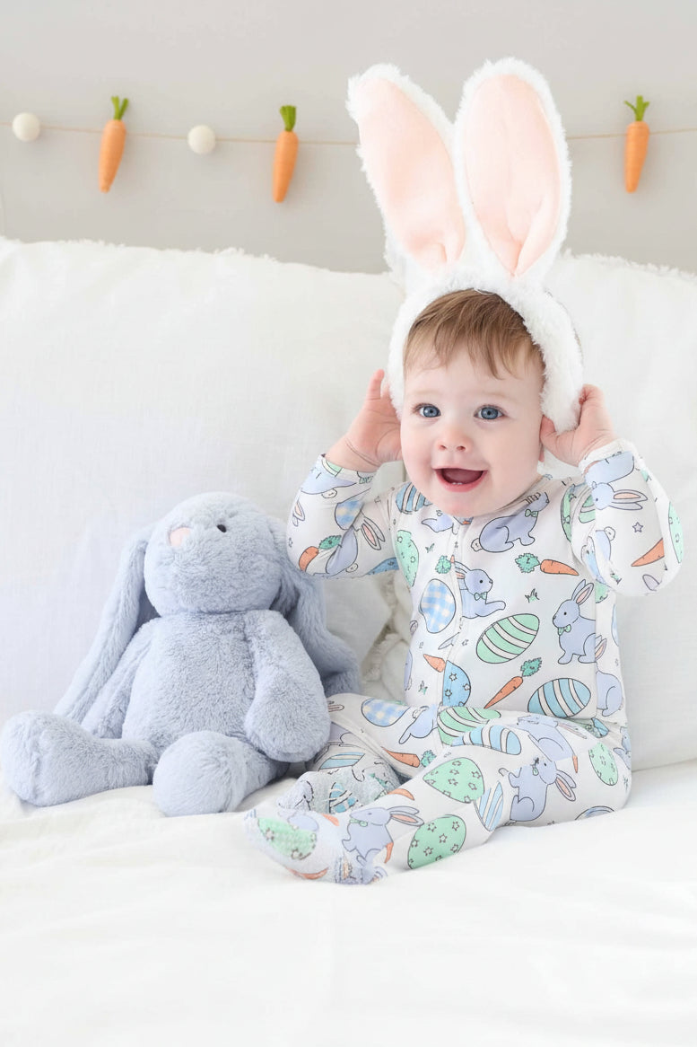 baby boy wearing a blue zipper footie pajama with bunny ears next to a light blue stuffed animal bunny 