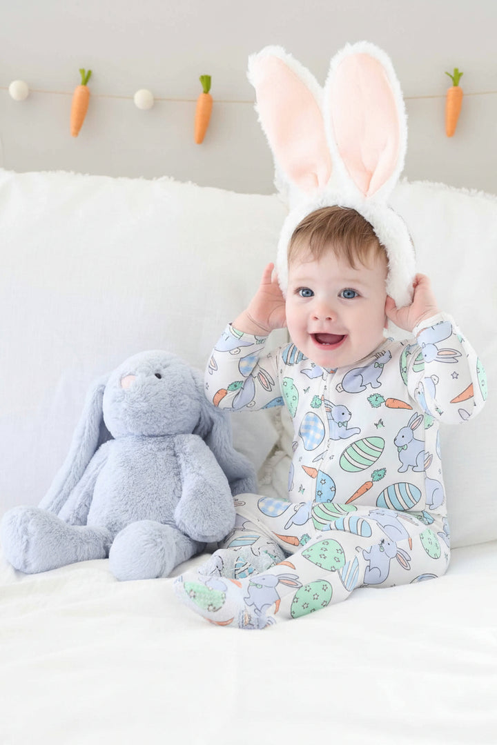 baby boy wearing a blue zipper footie pajama with bunny ears next to a light blue stuffed animal bunny 