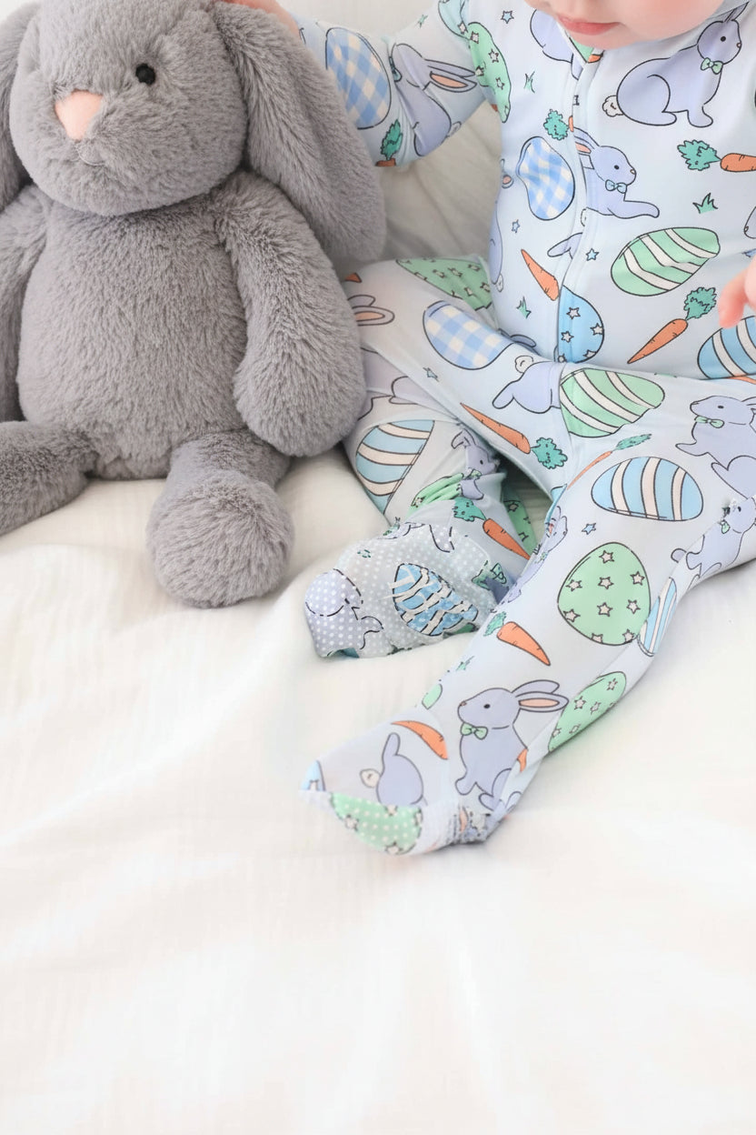 closeup of blue baby easter footie pajama with grips on the feet with a matching blue stuffed animal bunny 