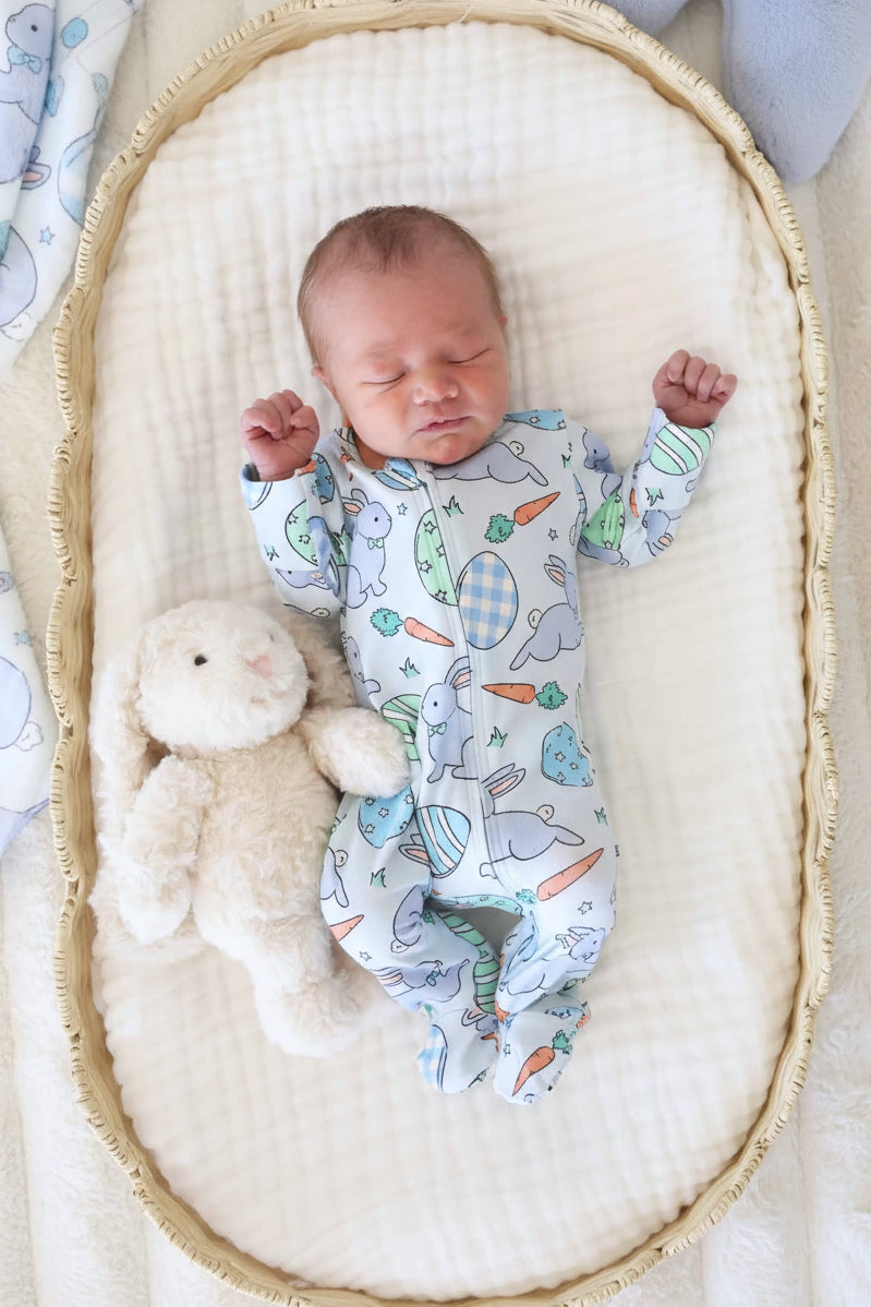 baby laying in basket wearing a blue easter footie next to a bunny stuffed animal