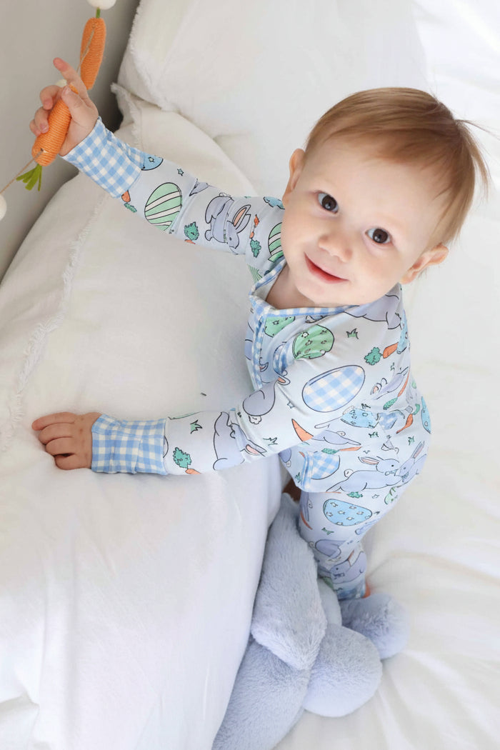 standing toddler wearing blue hoppy spring convertible zip romper holding a straw carrot
