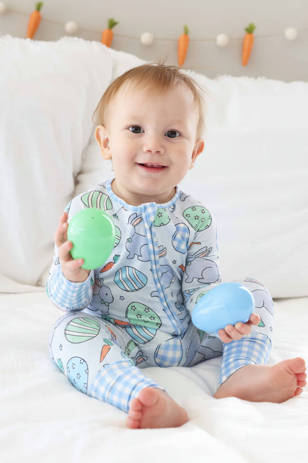 boy wearing a blue bunny and easter egg convertible zip romper pajama holding green and blue easter eggs 
