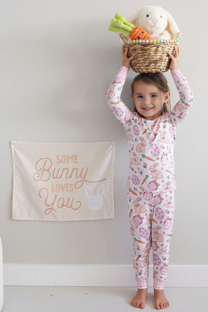 standing girl wearing the hoppy spring two piece pajama set with an easter basket on her head next to a some bunny loves you sign 