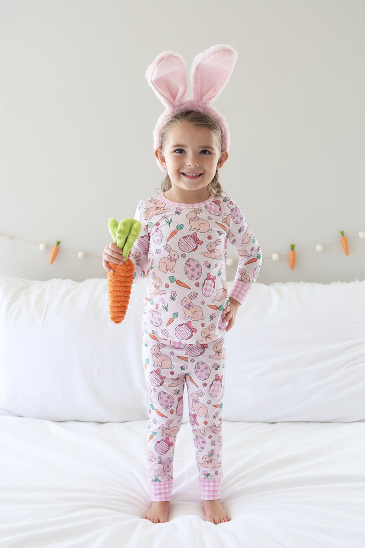 girl wearing pink easter pajama with a bunny ear headband and holding a stuffed carrot 