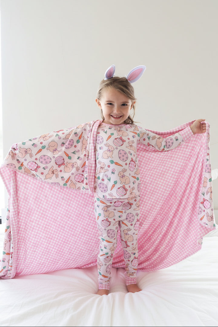 girl wearing the pink hoppy spring two piece pajama set with the matching double sided bamboo blanket draped over her shoulders 