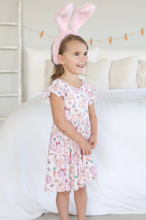 girl wearing a short sleeve knee length easter dress with bunnies, easter eggs and carrots on it wearing pink bunny ears 