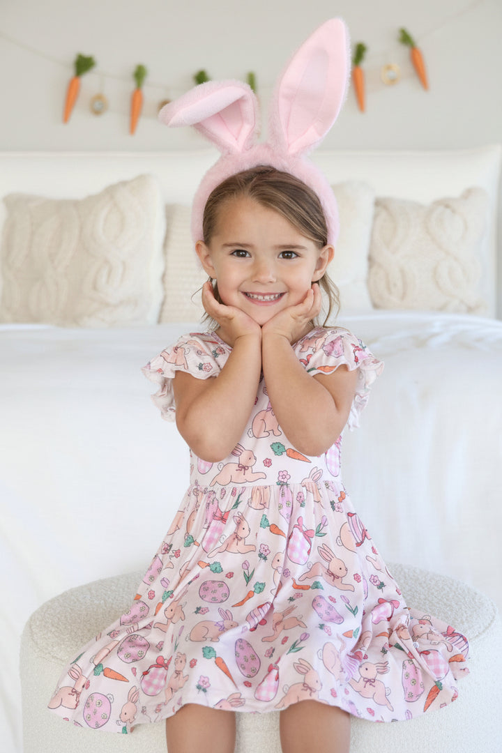 girl sitting where a ruffle sleeve knee length dress for girls in the pink hoppy spring print 